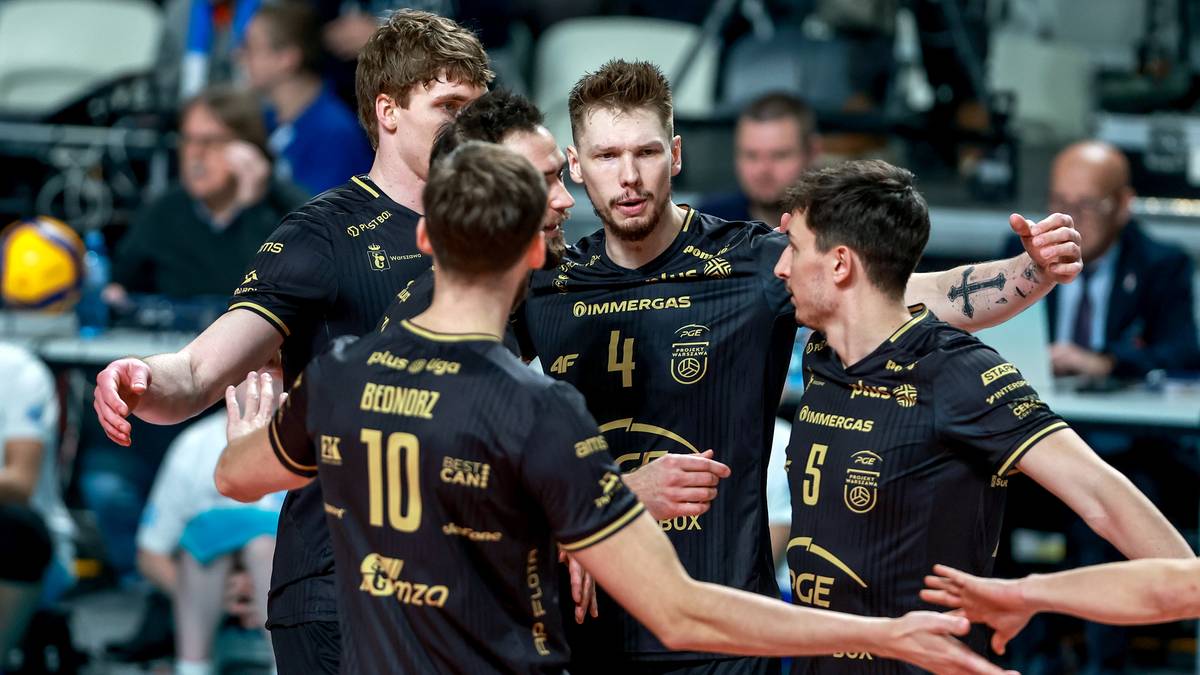 Grupa siatkarzy w czarnych strojach sportowych świętuje razem na boisku.