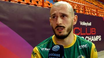 Mężczyzna z zarostem, ubrany w zieloną koszulkę sportową, odpowiada na pytanie trzymając przed sobą mikrofon z logo Polsat Sport. W tle widać trybuny stadionu i baner z napisem "Volleyball Club Champions".