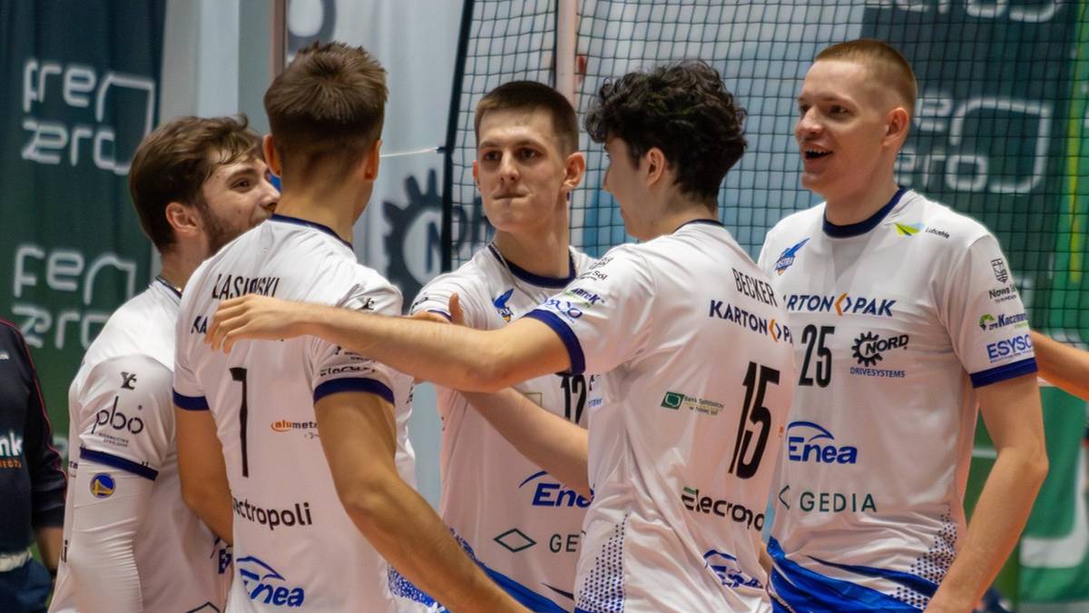 Siatkarze w białych strojach z niebieskimi detalami celebrują zdobyty punkt na boisku.