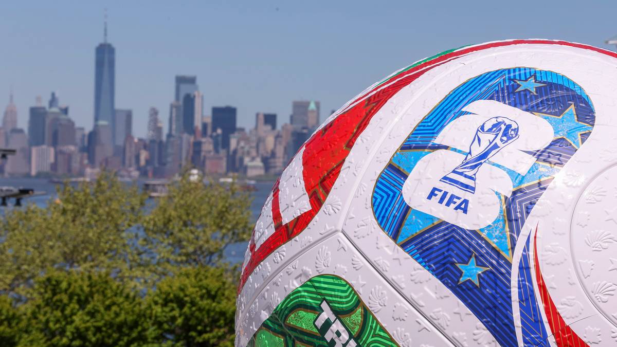 Zbliżenie na piłkę z logo FIFA, w tle panorama miasta.