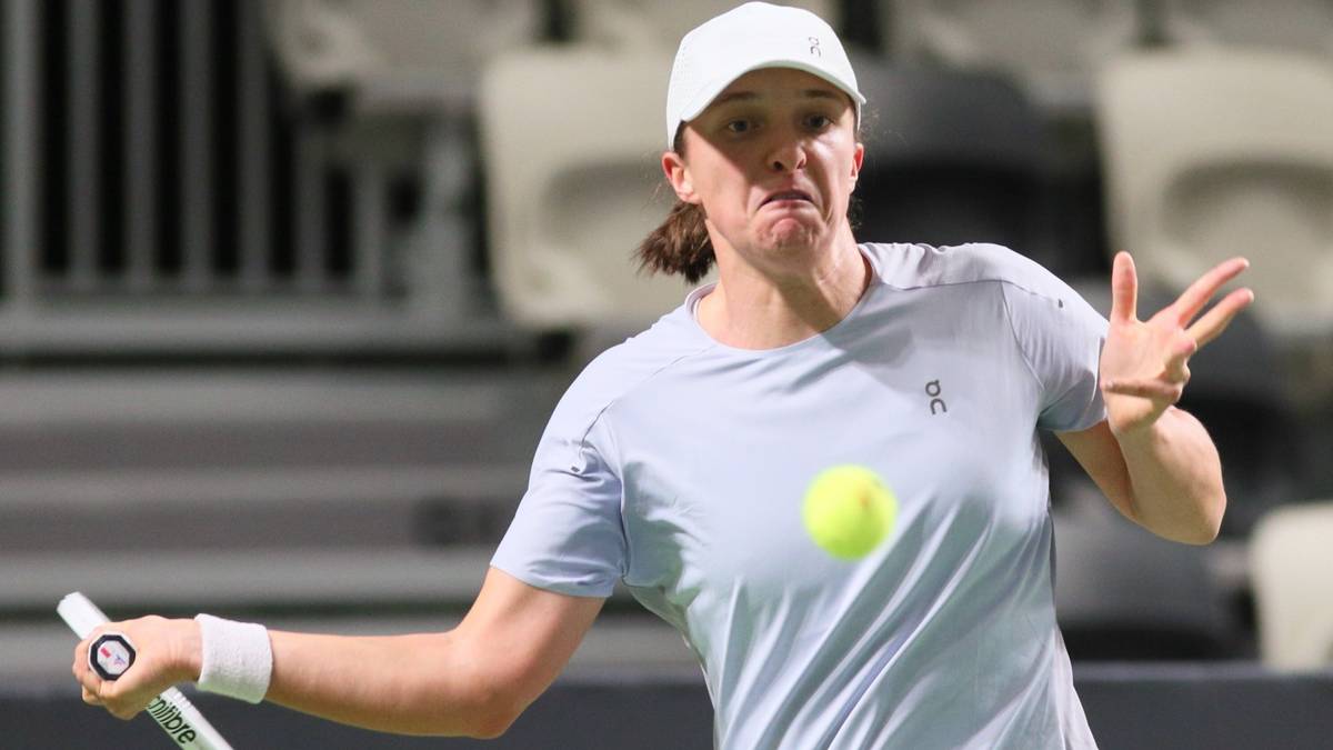 Tenisistka w szarym T-shircie i białej czapce, odbija piłkę rakietą.