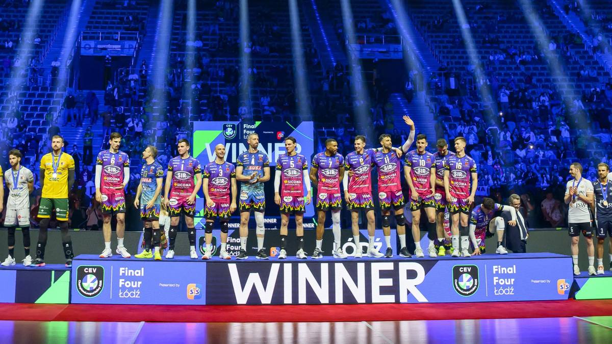 Siatkarze na podium, trzymający puchary i medale, w tle tłum i oświetlenie sceniczne.