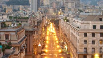Widok na ulicę w Genui z oświetlonymi latarniami i budynkami.