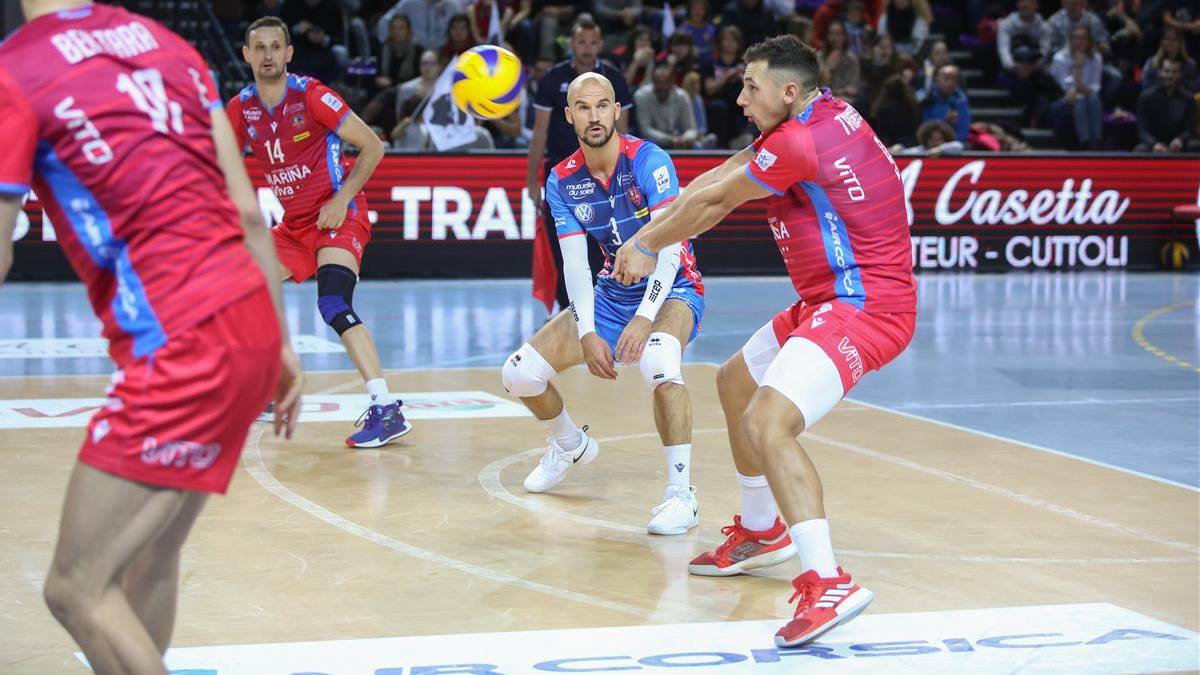 Siatkarze w czerwonych i niebieskich strojach rywalizują o piłkę na boisku podczas meczu.