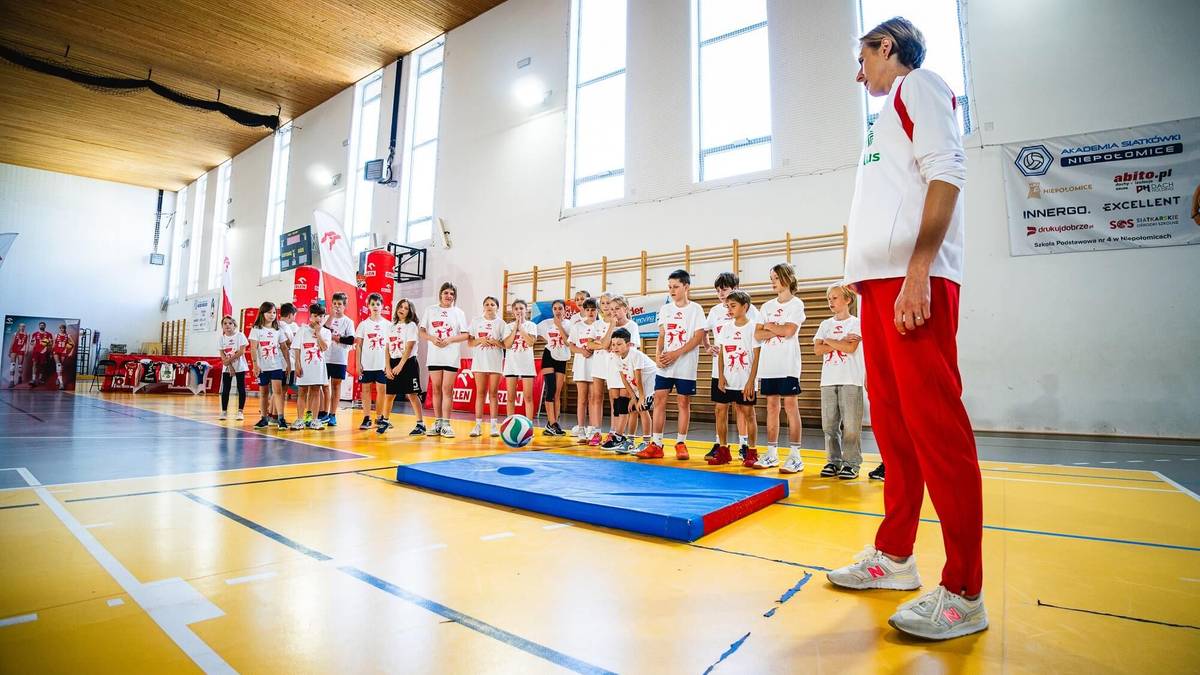 Siatkarz prowadzi zajęcia sportowe dla uczniów w sali gimnastycznej.