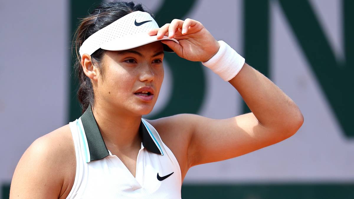 Tenisistka w białej bluzie i daszku z logo Nike, poprawia daszek na głowie.