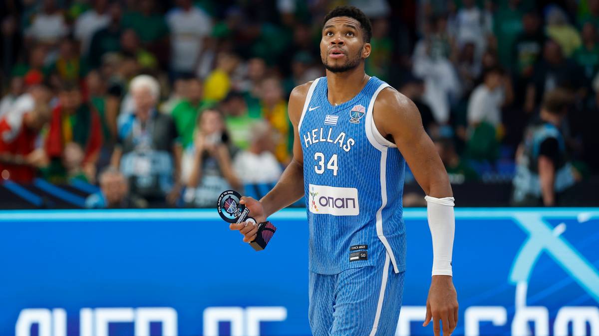 Koszykarz w niebieskim stroju z numerem 34 i napisem "HELLAS" trzyma przedmiot w ręce.