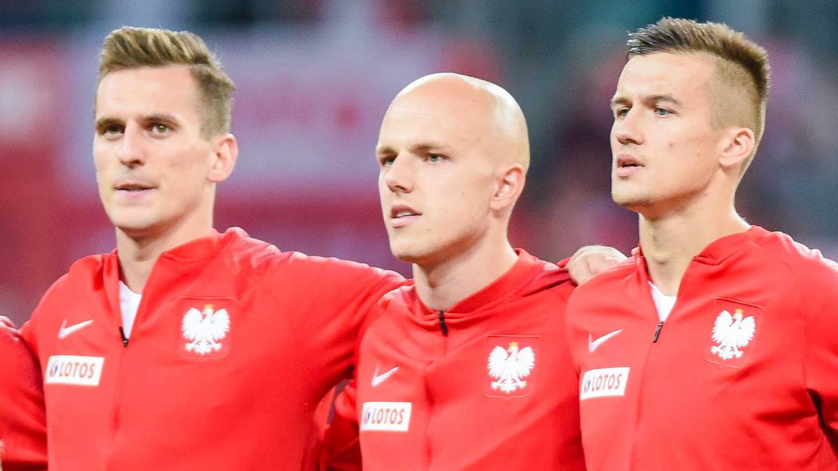 Trzech piłkarzy reprezentacji Polski w czerwonych koszulkach z godłem.