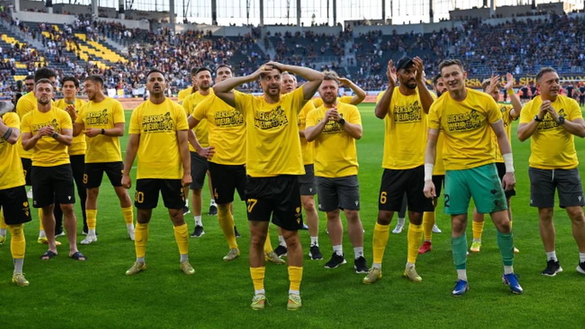 Piłkarze GKS w żółtych koszulkach stoją na boisku.