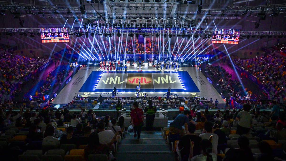 Widok hali sportowej podczas meczu Ligi Narod&oacute;w siatkarzy. Na niebieskim boisku widoczne logo VNL. Trybuny wypełnione publicznością, a nad nimi efektowne oświetlenie sceniczne.
