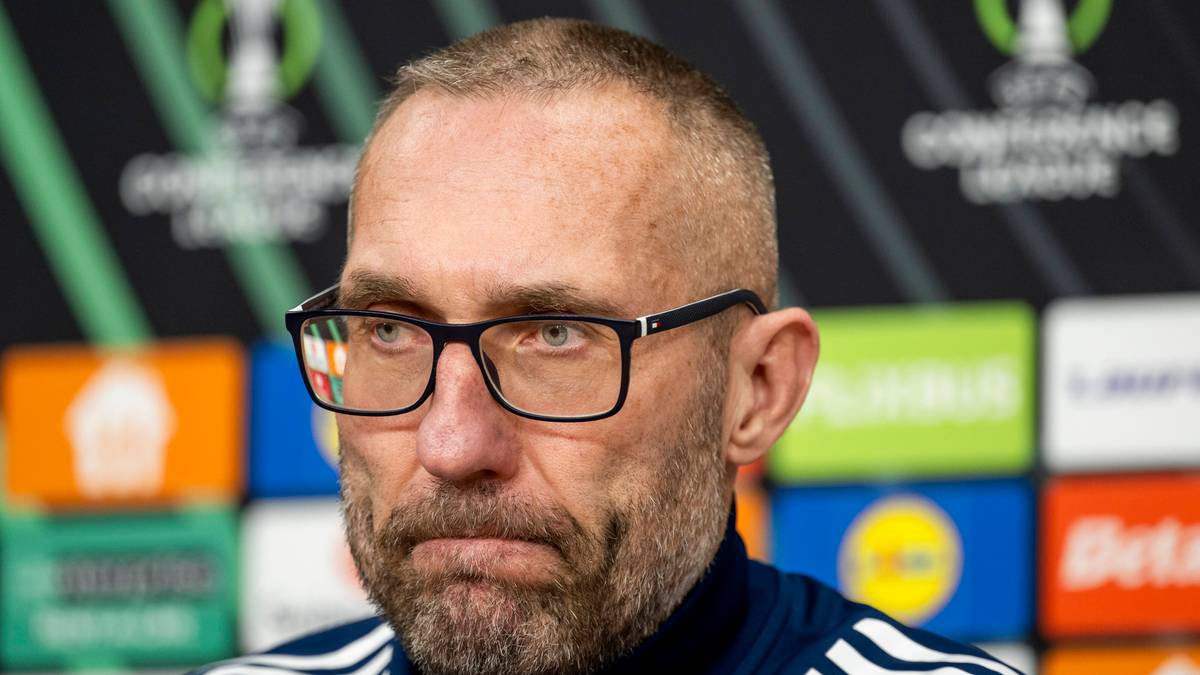 Portret mężczyzny w okularach z widocznym zarostem, ubranego w bluzę. W tle znajduje się seria kolorowych, podświetlonych plansz z logotypami.