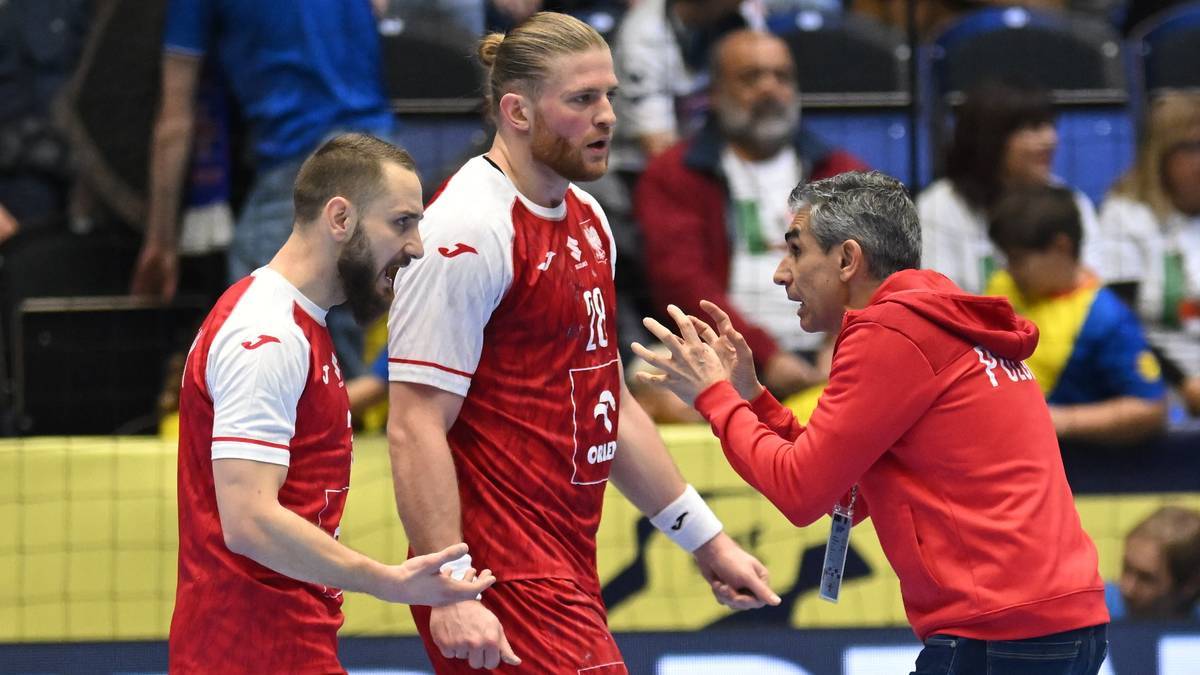 Dwóch zawodników w czerwonych strojach piłki ręcznej rozmawia z trenerem w czerwonej bluzie.