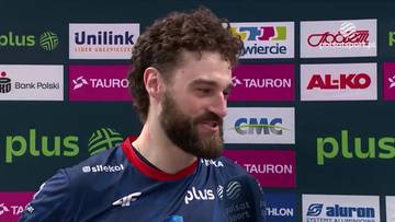 Mężczyzna z kręconymi włosami i brodą, ubrany w granatową koszulkę sportową z czerwonymi elementami. W tle widoczne są kolorowe logotypy sponsor&oacute;w, m.in. "Plus", "Unilink", "Tauron", "Al-ko".