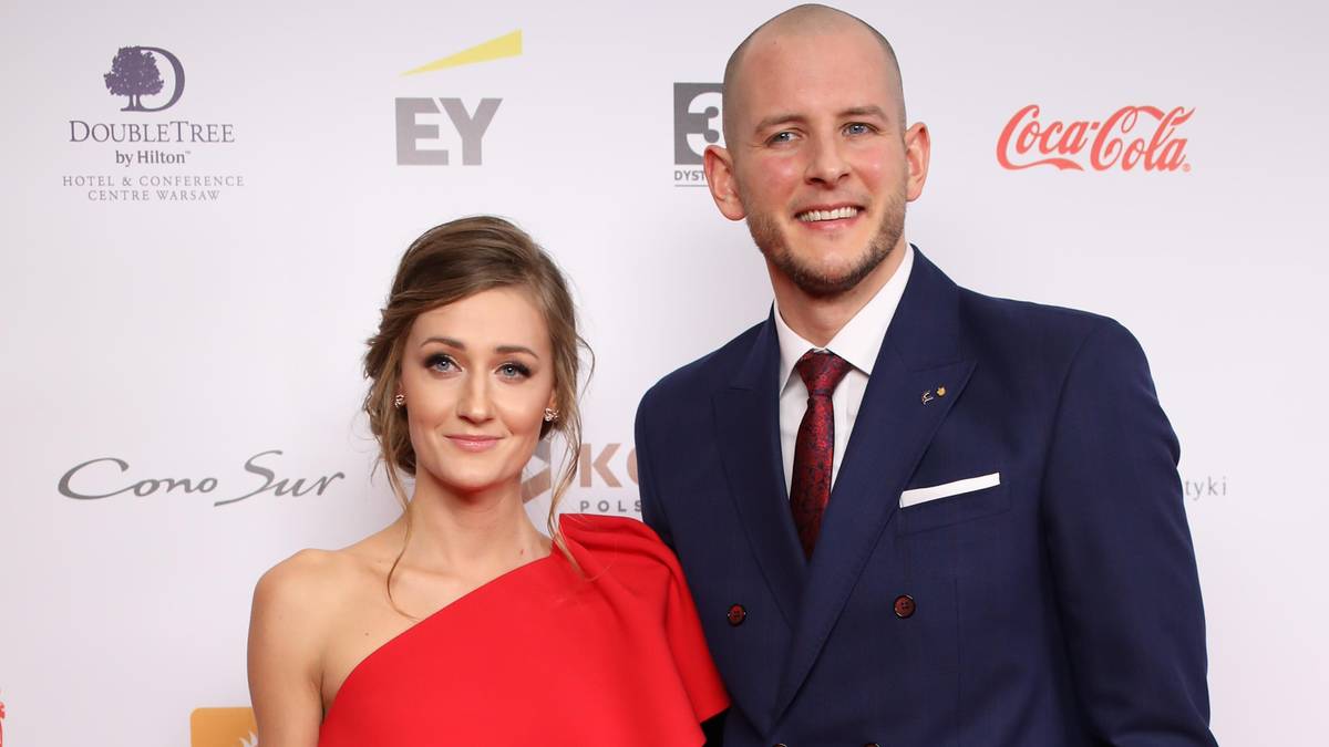 Bartosz Kurek i Anna Kurek pozują do zdjęcia w eleganckich strojach, uśmiechając się.