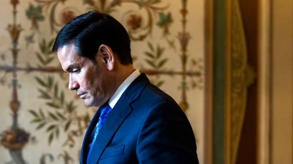 Mężczyzna w garniturze i krawacie pochyla głowę.