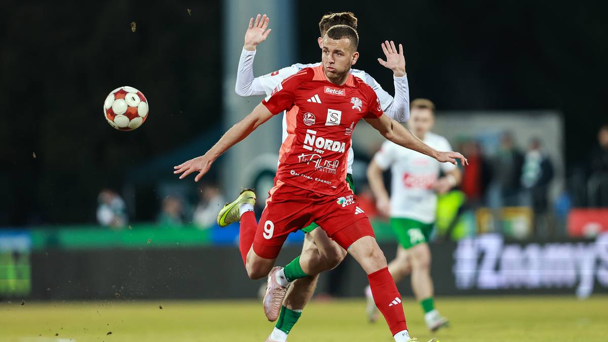 Piłkarz w czerwonej koszulce z numerem 9 pr&oacute;buje odebrać piłkę przeciwnikowi podczas meczu.