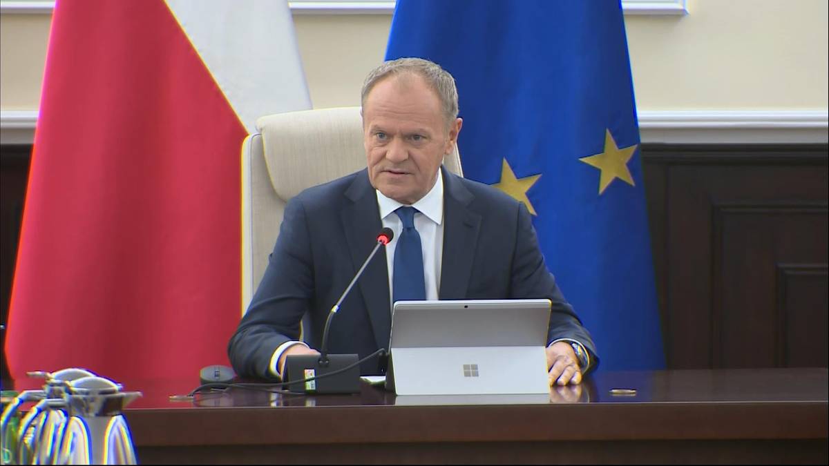 Prezydent siedzi przy stole, za nim flagi Polski i Unii Europejskiej.