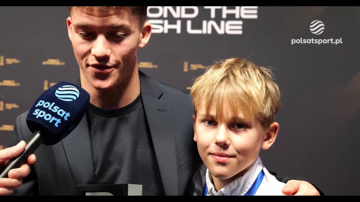 Młody mężczyzna trzymający mikrofon Polsat Sport obok młodego chłopca.