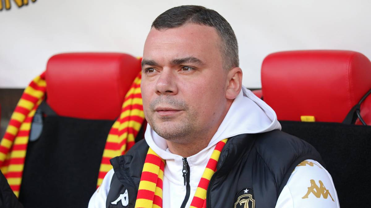 John Carver, trener Lechii Gdańsk, w szaliku klubowym, siedzi na ławce rezerwowych.