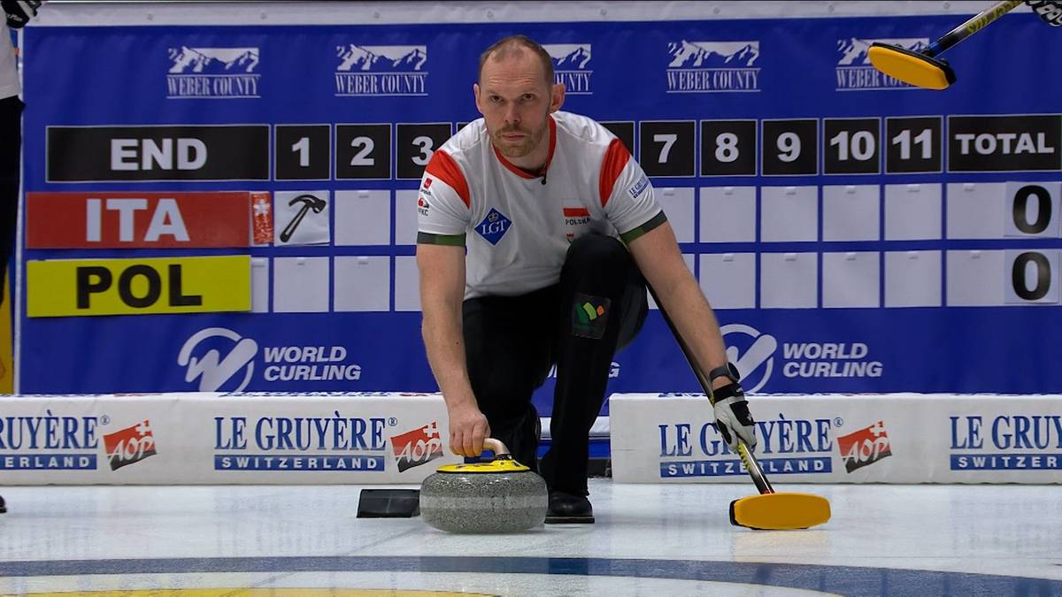 Gracz w curlingu wykonuje rzut kamieniem na lodowisku, w tle tablica wynik&oacute;w z wynikami meczu Polska-Włochy.
