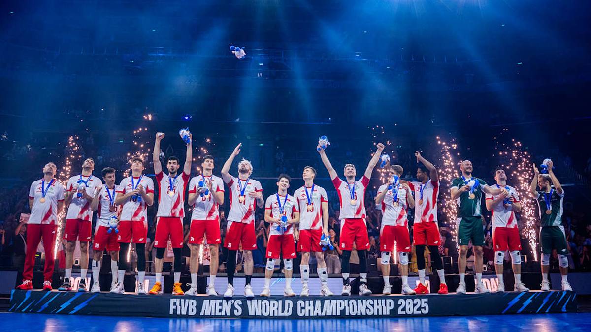 Drużyna siatkarzy w czerwonych strojach na podium, świętująca zwycięstwo. Trzymają medale i puchary, otoczeni konfetti i fajerwerkami.