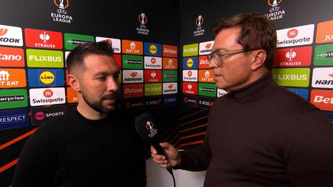 Dw&oacute;ch mężczyzn rozmawia na tle ścianki z logotypami sponsor&oacute;w Ligi Europy.