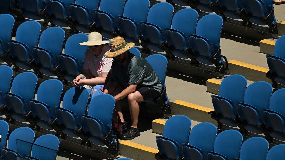 Dwóch widzów siedzących na pustych trybunach, oboje noszących kapelusze chroniące przed słońcem.