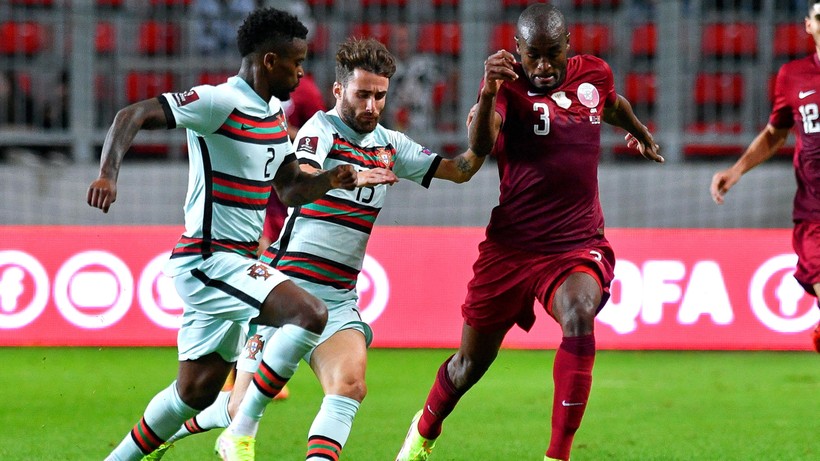 Dwóch piłkarzy w jasnych strojach z numerami 2 i 15 biegnie obok siebie, ścigając trzeciego piłkarza w ciemnym stroju z numerem 3.