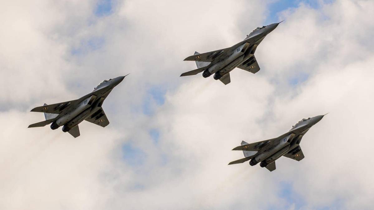 Trzy myśliwce wojskowe lecące w formacji na tle nieba z chmurami.