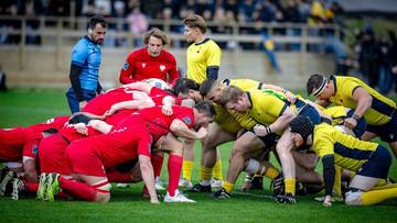 Zawodnicy rugby w czerwonych i żółtych strojach rywalizują o piłkę w trakcie akcji.