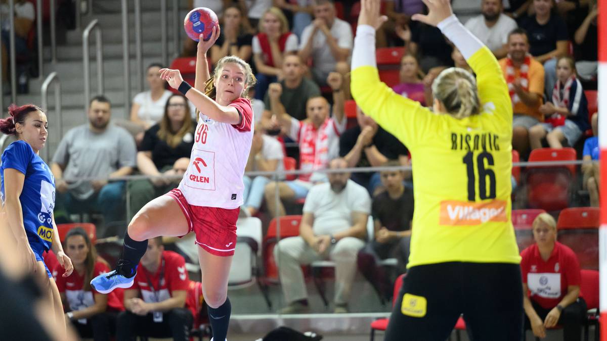 Piłkarka ręczna w białej koszulce i czerwonych spodenkach wykonuje rzut do bramki.