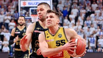 Dw&oacute;ch koszykarzy w trakcie meczu, jeden w ż&oacute;łtej koszulce z numerem 55 prowadzi piłkę, drugi w czarnej pr&oacute;buje go zatrzymać.