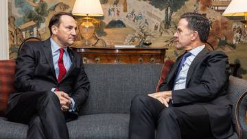 Dwóch mężczyzn w garniturach siedzi na kanapie, rozmawiając ze sobą.