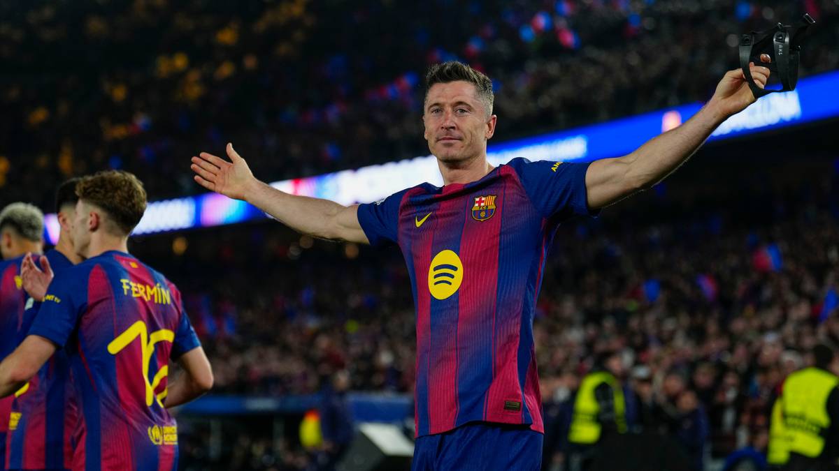 Piłkarz FC Barcelony Robert Lewandowski unosi ręce w geście triumfu na tle kibic&oacute;w.