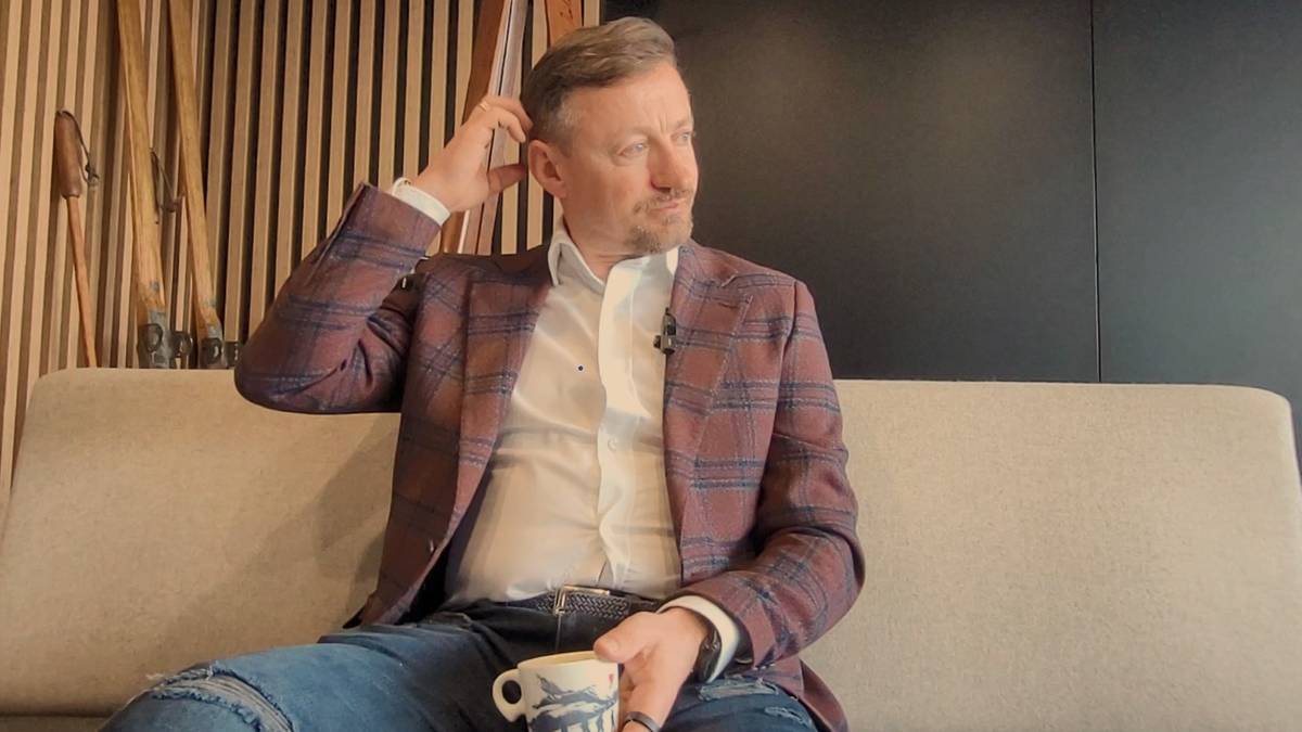 Mężczyzna w marynarce siedzi na kanapie z filiżanką w dłoni.