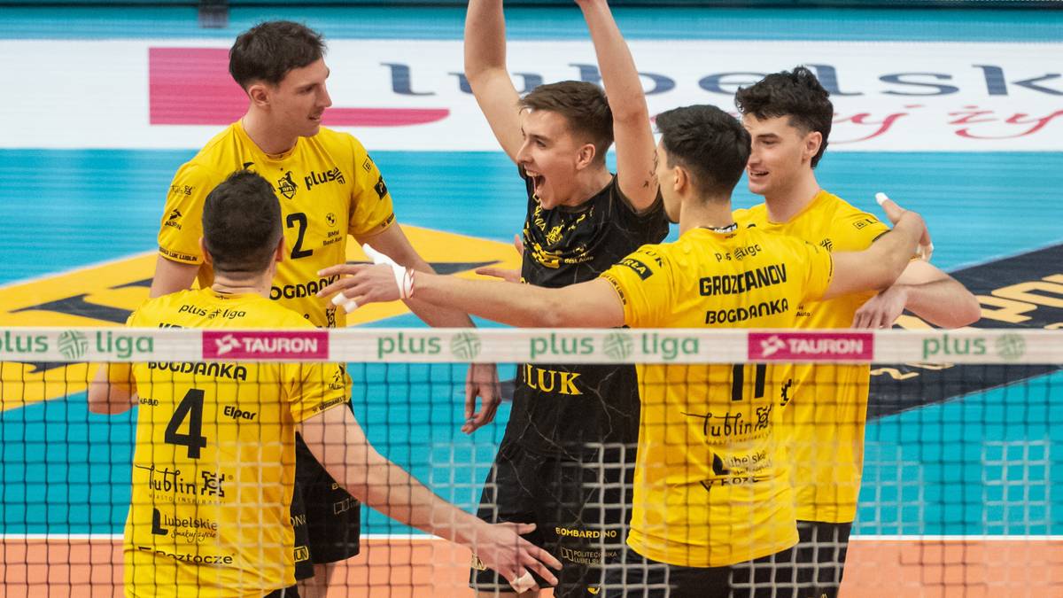 Sześciu siatkarzy w ż&oacute;łtych koszulkach świętuje zwycięstwo, z podniesionymi rękami w geście radości. Dw&oacute;ch z nich jest na pierwszym planie, patrząc w stronę obiektywu, a pozostali stoją za nimi.