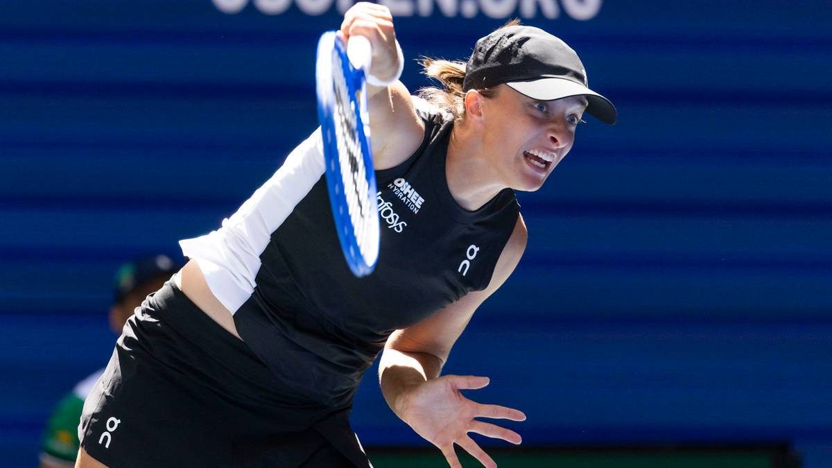 Tenisistka w czarnej koszulce i czapce z daszkiem, wykonująca zamach rakietą tenisową. Jej twarz wyraża skupienie i determinację.