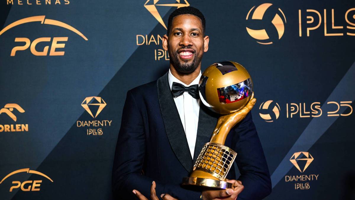 Mężczyzna w garniturze z muszką trzyma złote trofeum.