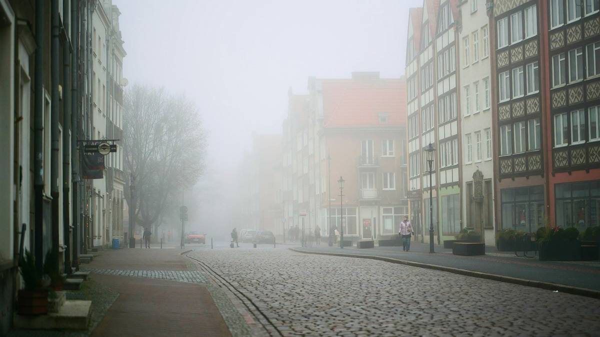 Ulica z kamienicami w gęstej mgle, ograniczona widoczność.