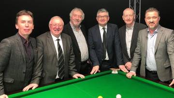 Grupa mężczyzn w garniturach stoi za stołem bilardowym.