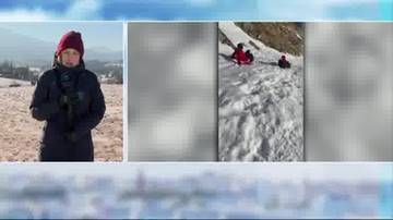 Kobieta w zimowym ubraniu stoi na tle zaśnieżonego krajobrazu g&oacute;rskiego, obok niej widoczne są fragmenty nagrania przedstawiającego osoby zjeżdżające na sankach po stoku.