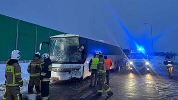 Miejsce wypadku z udziałem dw&oacute;ch autokar&oacute;w, widoczni ratownicy straży pożarnej i uszkodzone pojazdy na tle zimowego krajobrazu.