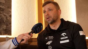 Mężczyzna z zarostem, ubrany w czarną bluzę z logotypami, udziela wywiadu trzymając mikrofon.