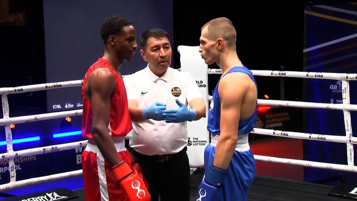 Dwóch bokserów w czerwonych i niebieskich strojach stoi naprzeciw siebie na ringu, rozdzielony przez sędziego w białej koszuli i niebieskich rękawiczkach.