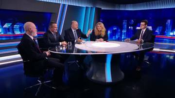 Pięć osób siedzi przy okrągłym stole w studiu telewizyjnym, dyskutując. Wszyscy są ubrani formalnie, a tło stanowi nowoczesna scenografia z niebieskimi światłami.