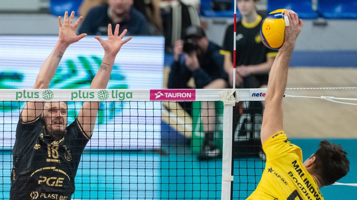 Siatkarz wykonuje atak nad siatką, a po drugiej stronie siatkarz pr&oacute;buje go zablokować.
