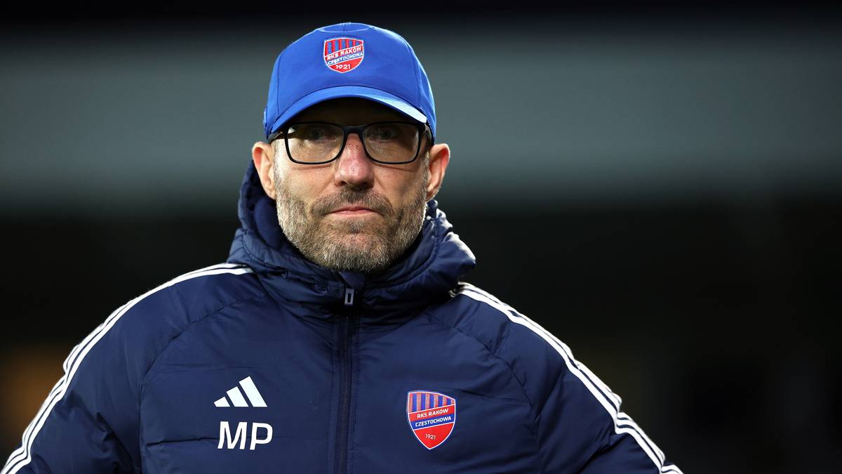 Mężczyzna w niebieskiej czapce z daszkiem i okularach, noszący ciemnogranatową kurtkę z logo Adidas i emblematem klubu sportowego.