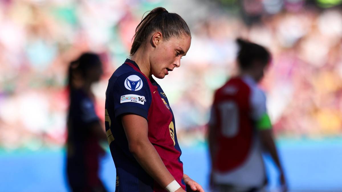 Piłkarka FC Barcelony z opuszczoną głową, w tle inne zawodniczki i trybuny stadionu.