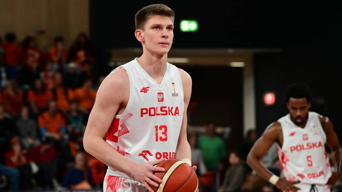 Polski koszykarz Jakub Szumert w białej koszulce z numerem 13 i napisem POLSKA, trzymający piłkę do koszyk&oacute;wki.