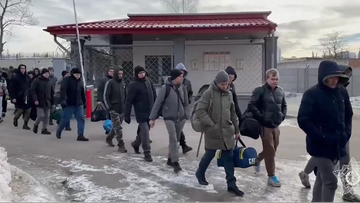 Grupa mężczyzn z torbami idzie w stronę bramy.